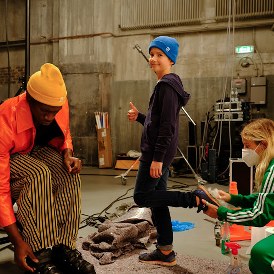 Junge trägt eine blaue Mütze und zeigt mit einem Daumen hoch zur Kamera und lächelt dabei . Neben ihn sind zwei Erwachsene